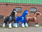 Three inflatable horse statues in black, blue, and brown against a brick wall.