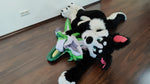 A small green Plop! dragon held by a border collie (fursuiter) on the floor. The dragon exploded and offers a view inside its body.